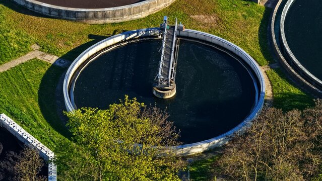 High angle aerial view of a circular clarifier basin at a modern wastewater treatment facility with rotating scraper bridge system. 