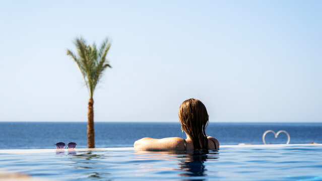 Woman relaxes in infinity pool, gazing at calm ocean