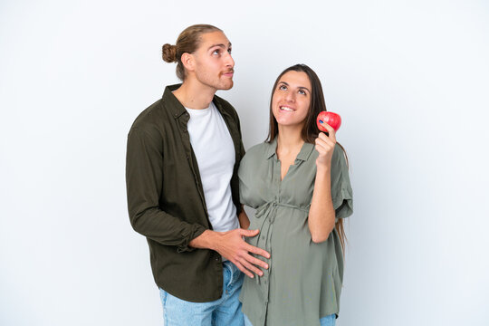 Young caucasian couple isolated on white background pregnant and frustrated while holding an apple