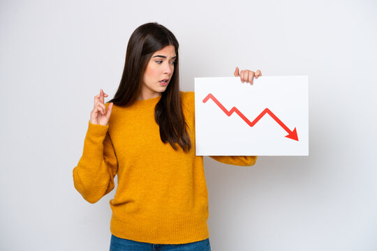 Young Brazilian woman isolated on white background holding a sign with a decreasing statistics arrow symbol with fingers crossing