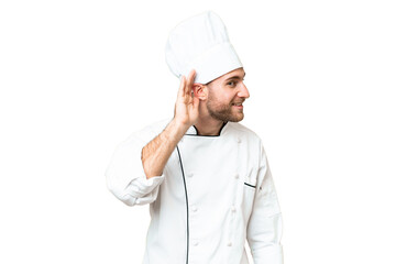 Naklejka premium Young blonde man Chef over isolated chroma key background listening to something by putting hand on the ear