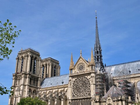 A wide architectural shot of Notre-Dame de Paris Cathedral featuring the iconic twin bell towers and the newly reconstructed spire (Fl&egrave;che) rising above the scaffolding. 