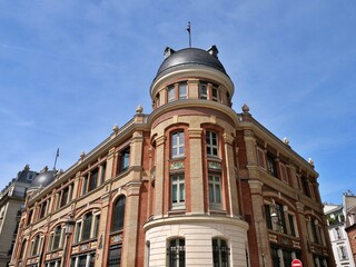 Obraz premium A low-angle shot of a stunning 19th-century eclectic building at the corner of Rue Massillon and Rue Chanoinesse in Paris. The architecture features a vibrant red brick facade, a rounded corner tower 