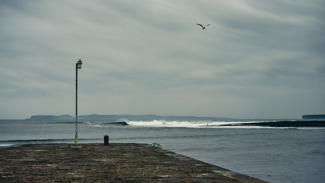 pier on the beach looking out to breaking waves and surfers in moody weather