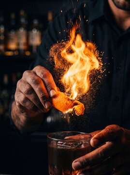 Bartender squeezing a flaming orange peel over a cocktail to create a fire burst
