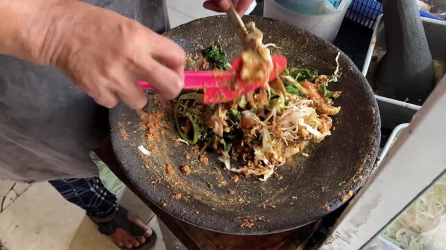 Close up of street food vendor hands preparing Lotek, Indonesian traditional vegetable salad with peanut sauce. Authentic Asian culinary preparation, healthy local food, and cultural heritage.