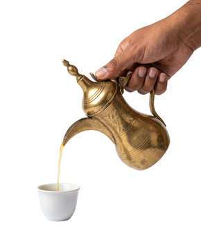 Hand pouring Saudi Arabian ghahwa coffee from traditional brass dallah into finjan cup