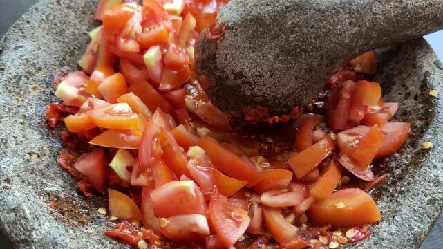 Close Up of Hand Grinding Fresh Red Tomato and Chili for Traditional Indonesian Sambal in Stone Mortar