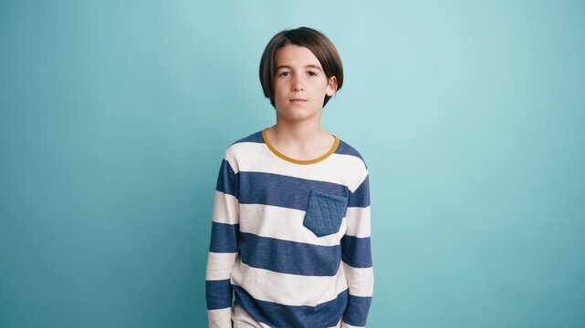 Portrait of a pre teen boy slowly opening his eyes and looking into the camera. He is standing against a solid colored studio background