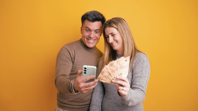 Excited man and woman celebrating a victory. They are taking a selfie with a smartphone while holding a fan of fifty euro banknotes