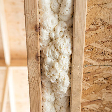 Close up of expanding spray foam insulation between wooden wall studs. Residential house construction and energy efficiency concept