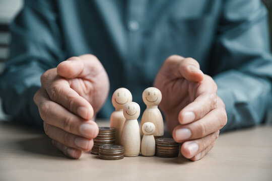Hands protecting wooden family figures with coins, representing family insurance, financial security, health coverage, savings plans and future protection.