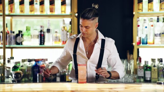 Handsome stylish bartender making a cocktail behind the bar counter. Skilled male professional pouring liquid into a glass and mixing it
