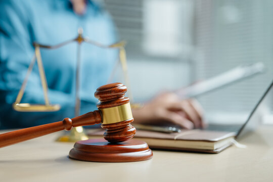 Judge gavel and justice scale on office desk with professional working on laptop, representing legal services, court decisions, compliance, law firm operations and judicial authority.