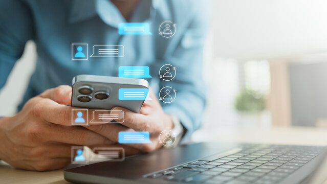 Professional using smartphone beside laptop with live chat icons, representing customer support, AI assistant and instant online communication for modern business service.