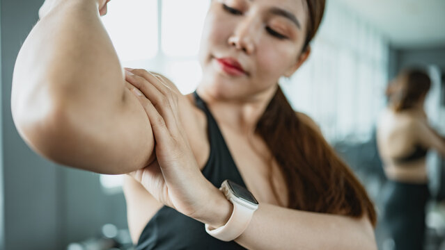 Asian fitness woman checking toned arm muscles after workout in gym. Strong bicep and body progress concept for training motivation, wellness and healthy lifestyle.