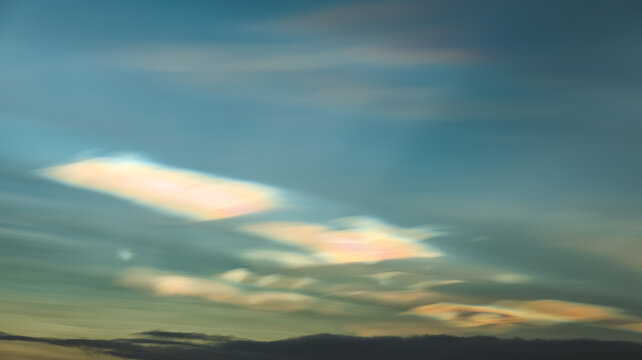 Rare iridescent nacreous cloud glowing in a pastel Arctic twilight sky above dark clouds, soft atmospheric winter scene in Norway