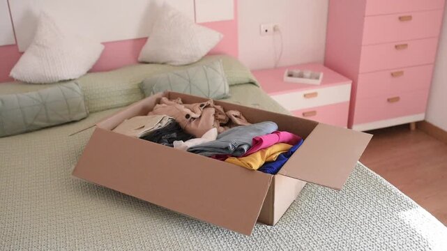 Video demonstrates process of packing things or unpacking after moving. Cardboard box filled with bright t-shirts and clothes symbolizes change, organized life, wardrobe decluttering or preparing for 
