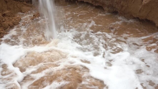 Close-up of a powerful water stream plunging into a foamy, muddy dirt basin, featuring authentic pump engine audio. Ideal dynamic B-roll for groundwater extraction, dewatering, and irrigation.