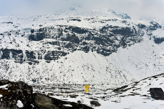 Frozen waterfalls on snow-covered Himalayan cliffs in North Sikkim, India, with a yellow prayer flag standing amid the rugged high-altitude winter landscape.