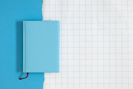 Blue hardback notebook with red bookmark ribbon on torn paper over blank math squared sheet background copy space overhead office stationery concept minimalist workspace flat lay mockup