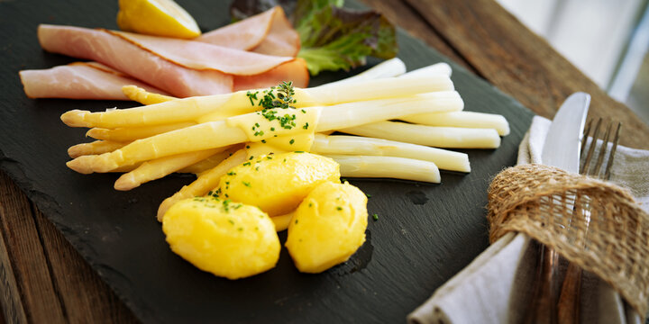 Seasonal white asparagus with creamy hollandaise sauce, served on a slate plate. Decoration suggestion for a modern seasonal cuisine. Close-up.