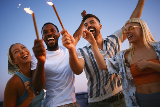 Diverse group of friends celebrating rooftop party with sparklers at sunset