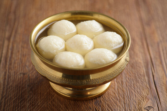 Sweet white rasgulla balls in a traditional brass bowl on wooden table
