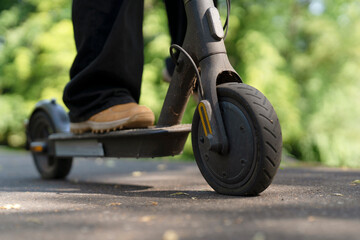 Person rides electric scooter on a path surrounded by green trees during daytime © Iryna