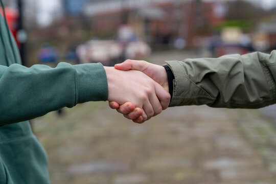 People shake hands in a city setting during a meeting on a cloudy day in the afternoon