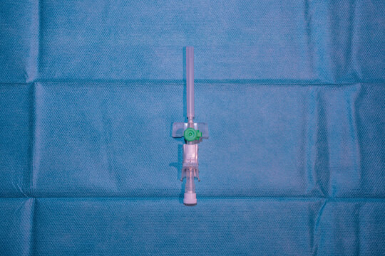 Single Green Peripheral Intravenous (IV) Cannula on Blue Sterile Medical Drape - Healthcare and Nursing Equipment
