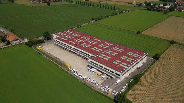 Cargo hub aerial view: An expansive industrial warehouse with a red roof sits amidst vast green fields, showcasing modern infrastructure and large-scale operations.