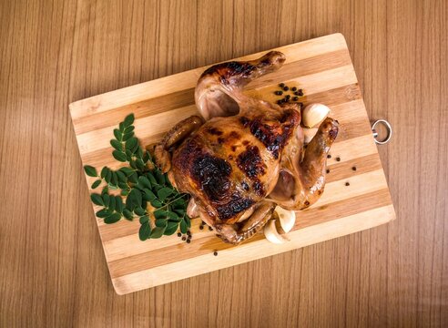 Whole spicy roasted chicken with garlic and herbs on wooden board