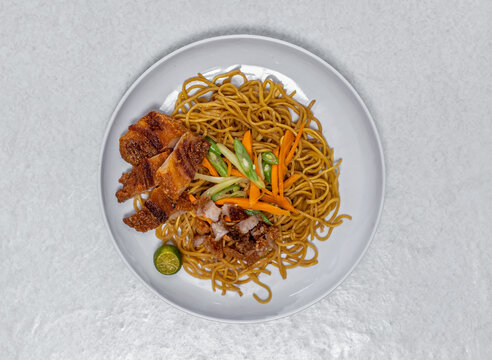 Filipino pancit canton noodles topped with crispy bagnet pork and fresh vegetables