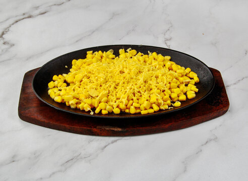 Hot sizzling corn topped with grated cheese on cast iron plate