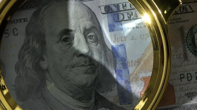 Portrait of Benjamin Franklin under magnifying glass on obverse of 100 dollar US bill close-up, banknote authenticity verification