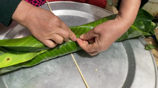 Traditional Tet preparation in Vietnam with hands tying banh tet using bamboo strings and green leaves for homemade festive food footage.