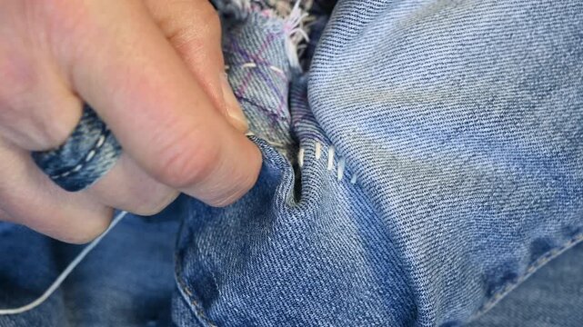 Extreme closeup shot of hands mending a hole in Jeans trousers with japanese Sashiko stitching technique.Upcycling clothes.