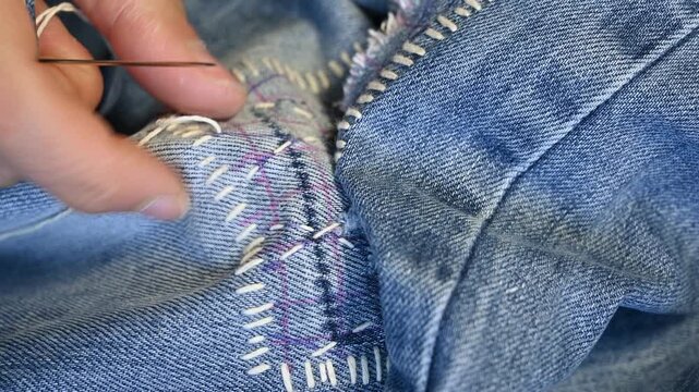 Extreme closeup shot of hands mending a hole in Jeans trousers with japanese Sashiko stitching technique.Upcycling clothes.