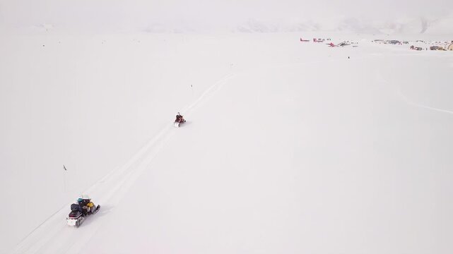 Aerial view of a remote research base with snowmobiles traversing the icy landscape