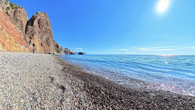 Beach ocean cliffs waves gently lap against a pebble shore under the bright summer sun at Cape Fiolent