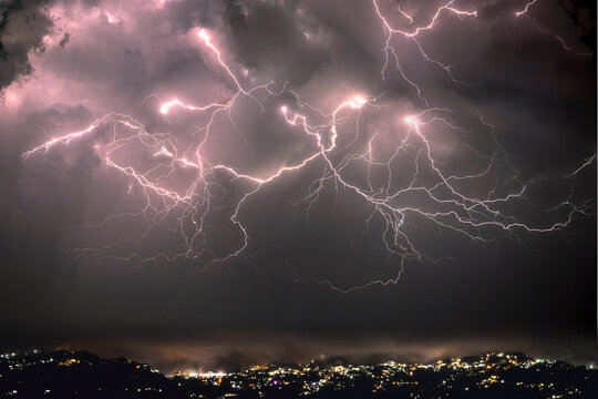 Dramatic lightning strikes illuminate a stormy night sky over a city