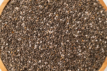 Naklejka premium Close-up of dry chia seeds in wooden bowl, top view. Food background, healthy seeds for breakfast, snacks, chia pudding. Superfood, texture of Salvia hispanica seeds 