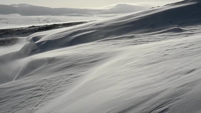 Dramatic snow blowing across a desolate, windswept mountain landscape