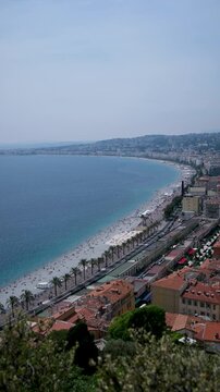 Aerial view of the promenade des anglais, the baie des anges and the crowded beach on a sunny day in nice, france, showcasing the beautiful coastline and mediterranean sea. Vertical video