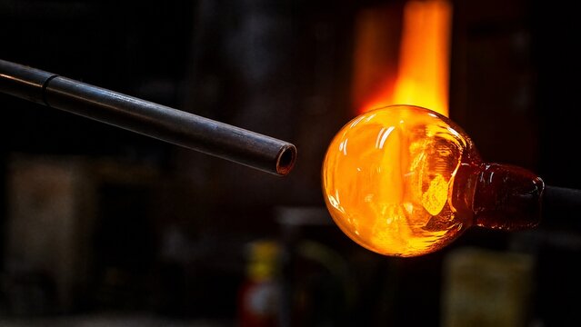 blowpipe. A slender metal blowpipe aimed at a glowing molten glass orb in a dark workshop. safety posters, maintenance manuals, designed for industrial assembly lines and welding operations.