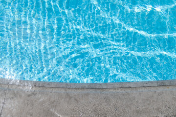 Curved stone swimming pool edge beside bright turquoise water with shimmering ripple reflections creating a calm minimalist resort background for summer travel wellness and leisure themes © Duncan