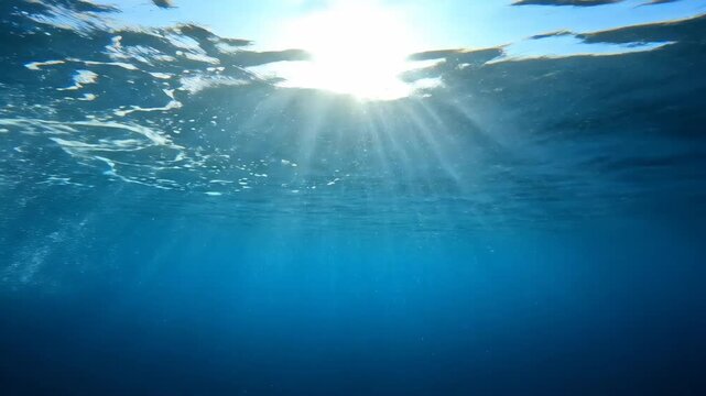 underwater view of bright sun rays piercing through clear blue ocean water. bubbles rising to surface. marine environment, scuba diving concept. abstract nature background, summer recreation.