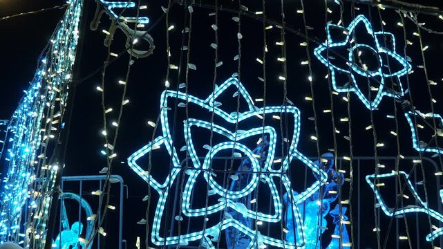 Enjoying Christmas Night With Sparkling Garlands and Shining Snowflakes in the City. The city is filled with bright Christmas garlands and sparkling lights. Snow falls gently as people admire the fest