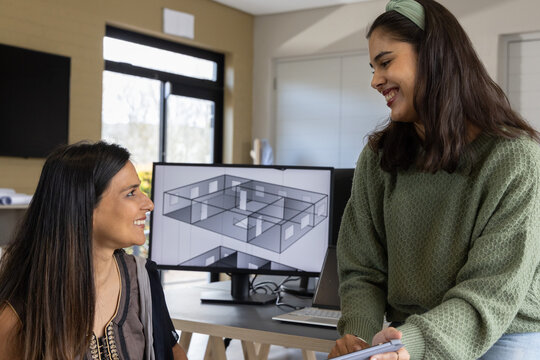Diverse female colleagues collaborating at modern office desk, examining 3D floor-plan on monitor